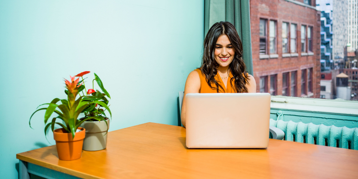 Woman in orange shirt sitting behind laptop