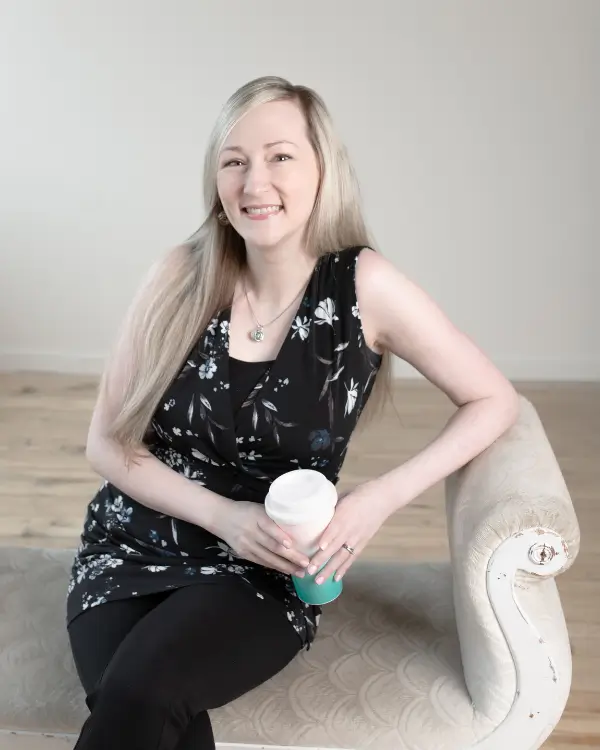 Kari smiling sitting on ottoman holding a coffee cup